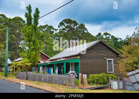 Semplice cottage in legno con lavatoio appeso al portico e alti alberi sullo sfondo in una piccola città australiana Foto Stock