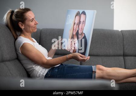 Donna di mezza età con una foto stampata su una tela tra le mani. Ritratto dei suoi figli per essere presto appeso al muro. Foto Stock