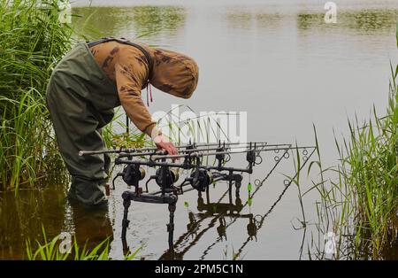 Fisherman con i wader piegati sopra la sua canna e le bobine nell'acqua. Foto Stock