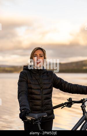 giovane donna che guarda la macchina fotografica, sorridendo con la sua bicicletta Foto Stock
