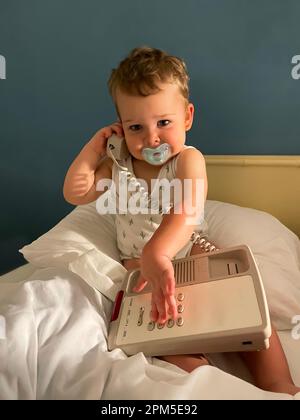 bambino con succhietto e telefono sul letto che guarda dentro la fotocamera Foto Stock