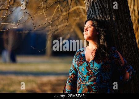 Una bella donna si appoggia all'albero in luce dorata, Foto Stock