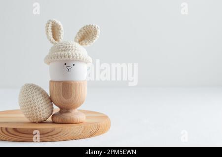 uovo di pasqua in cappello all'uncinetto con orecchie da coniglio in portuovo di legno Foto Stock