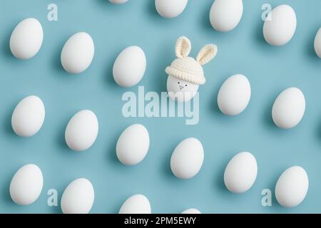 uovo di pasqua in cappello a uncinetto con orecchie da coniglio su sfondo blu. Posizione piatta Foto Stock