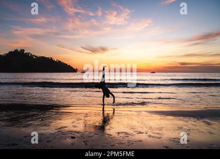 Persona che fa la ruota di cart attraverso una spiaggia in Costa Rica al tramonto. Foto Stock