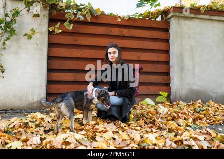 giovane donna in un cappotto con un cane in una passeggiata vicino alla casa Foto Stock