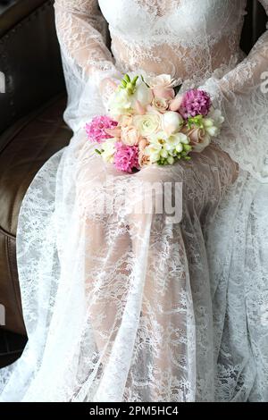 una giovane sposa in un pizzo bianco peignoir tiene in mano un bouquet di fiori da sposa. Bouquet di nozze in pizzo di una ragazza. beautifu Foto Stock