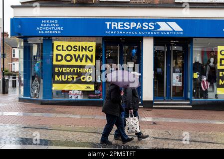 Persone a Southend su Sea High Street con ombrelloni, passando chiudere in giù per il negozio di abbigliamento all'aperto. Vacanza in riva al mare con piogge lunedì. Negozio in difficoltà Foto Stock