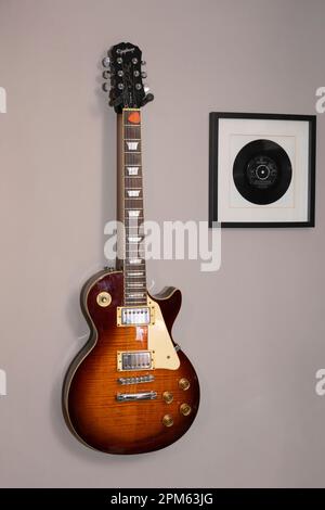 Una classica chitarra elettrica Les Paul Epiphone Standard appesa a una parete accanto a un disco in vinile incorniciato di You'll Never Walk Alone, Regno Unito Foto Stock