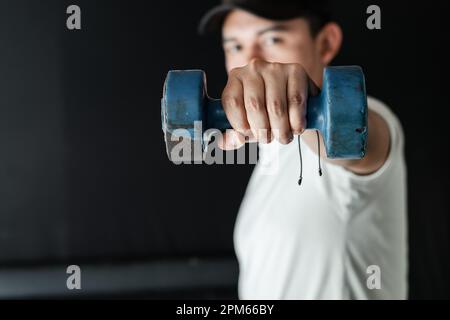 Primo piano della mano di un Latino che tiene un manubrio blu, lavorando alla resistenza muscolare. Foto Stock