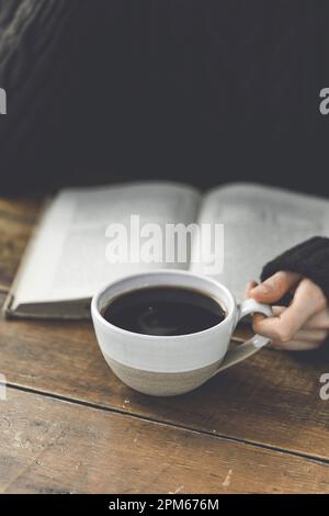 Una mano donna che tiene un caffè nero con un libro di lettura Foto Stock