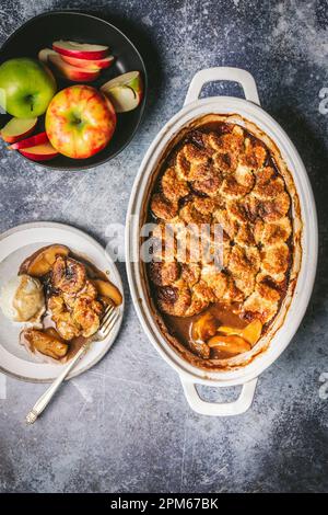 Cobbler di mele in teglia da forno in ceramica con servizio su piatto con gelato alla vaniglia e ciotola di mele fresche Foto Stock