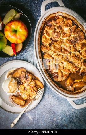 Cobbler di mele in teglia da forno in ceramica con servizio su piatto con gelato alla vaniglia e ciotola di mele fresche Foto Stock