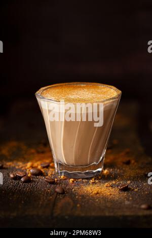 Un bicchiere resistente al calore che contiene una bevanda dolce con latte e cannella macinata. Foto Stock