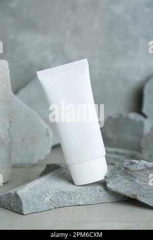 Tubo di crema per le mani tra le pietre su sfondo grigio. Modello per il design Foto Stock