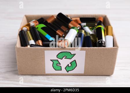 Batterie usate in scatola di cartone con il simbolo di riciclaggio su un tavolo di legno bianco, primo piano Foto Stock