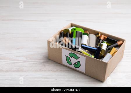 Batterie usate in scatola di cartone con il simbolo di riciclaggio su un tavolo di legno bianco, spazio per il testo Foto Stock