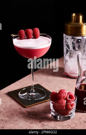 Cocktail Clover club in un alto coupé di vetro guarnito con tre lamponi su una raccolta d'oro. Foto Stock