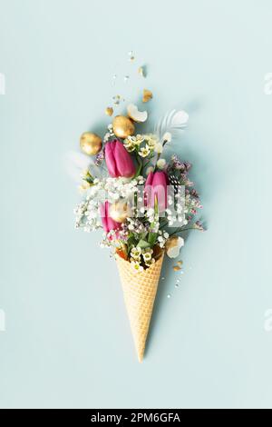Composizione pasquale. Cono gelato con bellissimi fiori e uova di pasqua dorate su fondo blu piatto Foto Stock