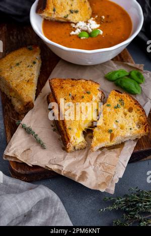 Panini al formaggio alla griglia guarniti con timo e una ciotola di zuppa di pomodoro dietro di loro. Foto Stock