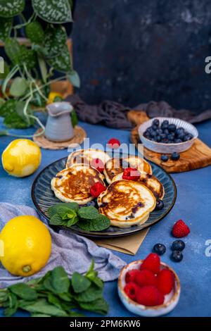 Frittelle al mirtillo al limone guarnite con mirtilli e lamponi su un piatto scuro. Foto Stock