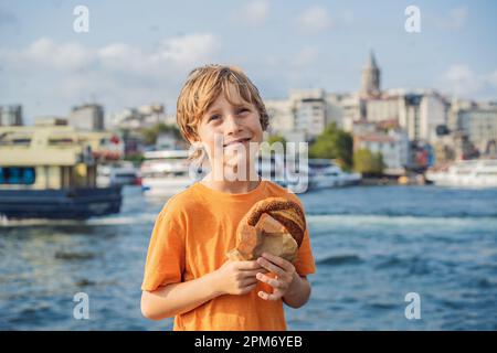 Ragazzo a Istanbul che faceva colazione con Simit e un bicchiere di tè turco. Bicchiere di tè turco e bagel Simit contro la baia del corno dorato e la Galata Foto Stock