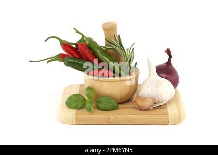 Spezie, erbe aromatiche e tema ancora vita con peperoncino in mortaio di legno, cipolla rossa, pepe nero, rametto basilico e bulbo d'aglio isolato su Whi Foto Stock