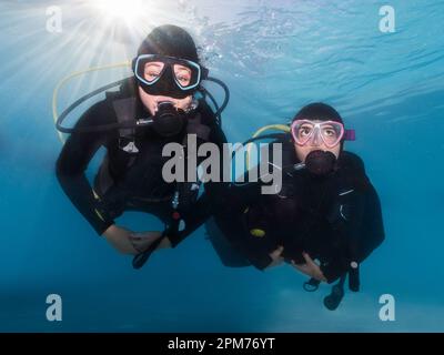 Primo piano di due subacquei che nuotano sott'acqua verso la macchina fotografica con i raggi luminosi che brillano attraverso la superficie dell'acqua dietro di loro Foto Stock