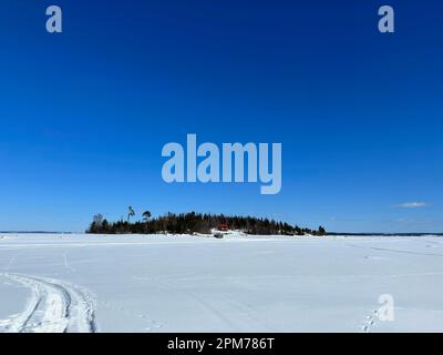 Isola remota con cabina rossa coperta di neve sotto un cielo azzurro e limpido nel nord della Svezia Foto Stock