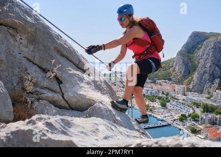 Donna sale via ferrata Fortica, sopra la città di Omis, Croazia, in estate. Arrampicatore, avventura, attivo, turismo. attività. Foto Stock