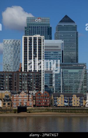 I grattacieli di Canary Wharf, parte del quartiere centrale degli affari di Londra, dominano le abitazioni sul fiume Tamigi. Cielo blu e nuvola bianca. Foto Stock
