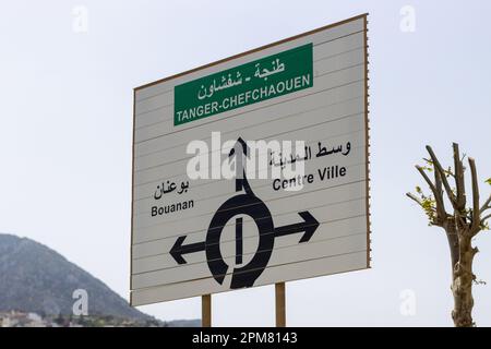 Grande cartello stradale in Marocco con tre frecce che indicano le indicazioni per Tangeri - Chefchaouen, centro città e Bouanane, insieme a una rotatoria e un tu Foto Stock