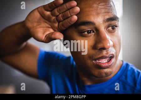 Primo piano di un giovane biraciale stanco che pulisce il sudore dalla fronte mentre si esercita in palestra Foto Stock