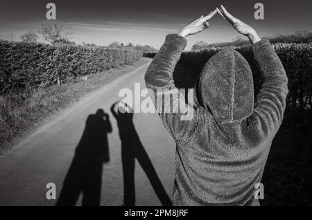 Una donna colpisce una posa per formare ombre allungate di una coppia mentre camminano lungo una corsia di campagna a Billingshurst, West Sussex, UK, la sera. Foto Stock