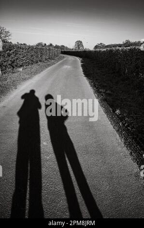 Le ombre allungate di una coppia mentre camminano lungo una corsia di campagna a Billingshurst, West Sussex, Regno Unito, la sera. Foto Stock