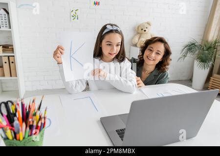 Genitore overjoyed che guarda il laptop vicino alla figlia con lettera che ha video lezione di terapia vocale a casa, immagine di scorta Foto Stock