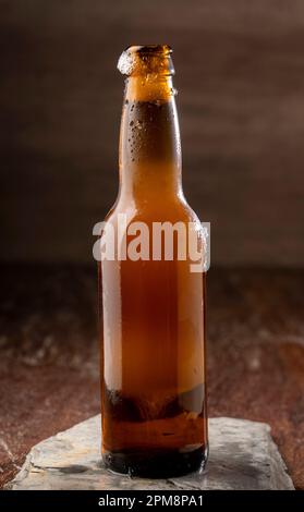 Una bottiglia di birra fredda su una roccia grigia su uno sfondo bianco Foto Stock