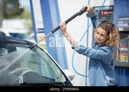 giovane donna che pulisce la sua auto in una cabina self service Foto Stock