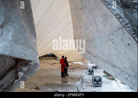 Wunsiedel, Germania. 12th Apr, 2023. Due persone stanno sotto il tetto della tenda, che è in parte sollevato nell'aria. Il tetto della tenda di 1600 metri quadrati, originariamente progettato dall'architetto Frei otto, è innalzato sopra l'auditorium del Festival Theater. Credit: Daniel Vogl/dpa/Alamy Live News Foto Stock