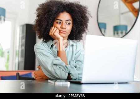 Una donna annoiata sente mancanza di motivazione, un dipendente remoto che si sente stanco perché manca di interesse per l'attività corrente, seduto di fronte al notebook, il mento a riposo con la mano in ufficio Foto Stock