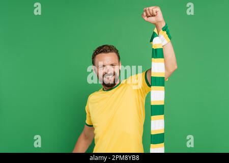 allegro tifoso di calcio in t-shirt gialla con sciarpa a righe e guardando la macchina fotografica isolato su verde, immagine stock Foto Stock