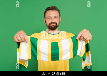 tifoso di calcio bearded in t-shirt gialla con sciarpa a righe e guardando la macchina fotografica isolato su verde, immagine stock Foto Stock