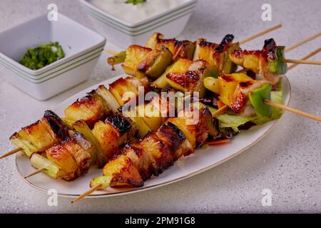 Kebab di maiale e ananas tradizionali su bastoncini con una salsa a lato per guarnire. Foto Stock