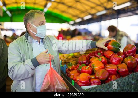 Uomo in maschera acquistare pepe nel mercato Foto Stock