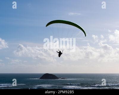 Un parapendio vola su una scena oceanica con un Island.Backlit silhouette.Sport.Recreation Foto Stock