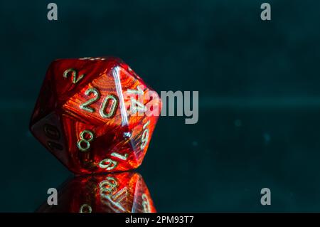 Immagine ravvicinata di un dado rosso a 20 lati che gioca a ruolo su una superficie riflettente Foto Stock