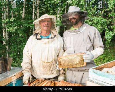 Ritratto di due apicoltore maschi che lavorano in un apiario vicino ad alveari con api. Raccogliere il miele. Apicoltore in apiario. Concetto di apicoltura. Foto Stock