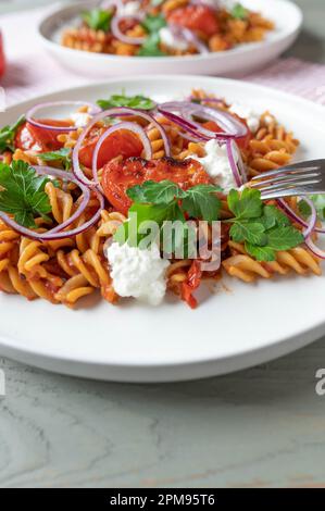 Pasta di grano integrale con salsa di pomodoro, pomodori arrostiti e ricotta, farcitura di cipolla rossa. Piatto vegetariano sano e a basso contenuto di grassi Foto Stock