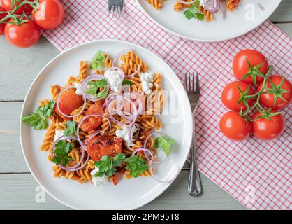 Piatto di pasta vegetariano con tagliatelle a grani interi, salsa di pomodoro, ricotta, pomodori arrosto, cipolle rosse su un piatto Foto Stock