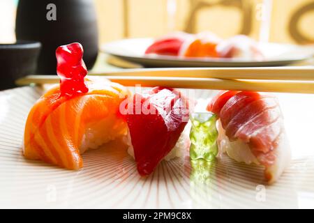 Orsacchiotti gummici che suonano su un tavolo da pranzo con tre nigiris sushi. Foto Stock